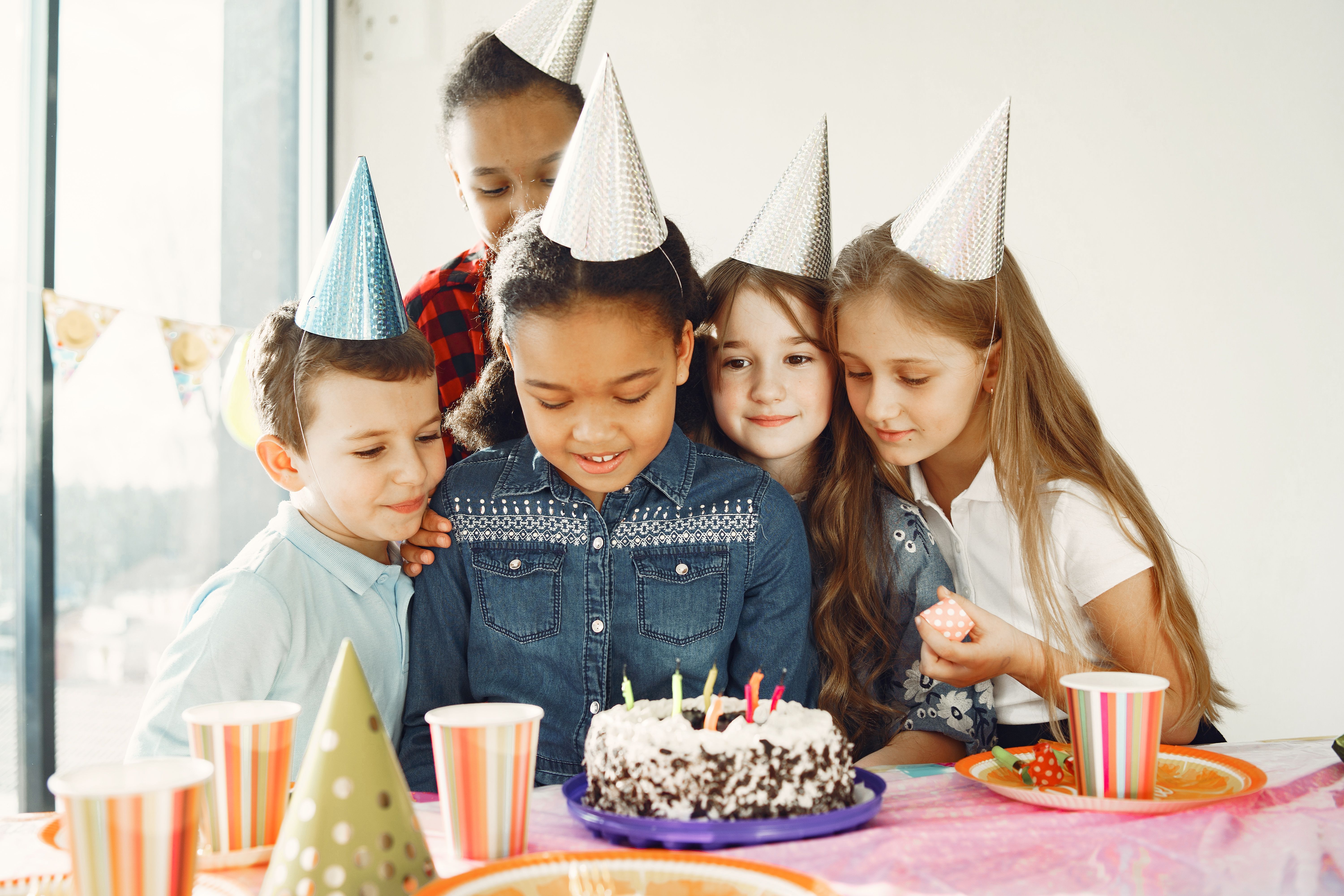 Kids in party hats gathered around a birthday cake with lit candles